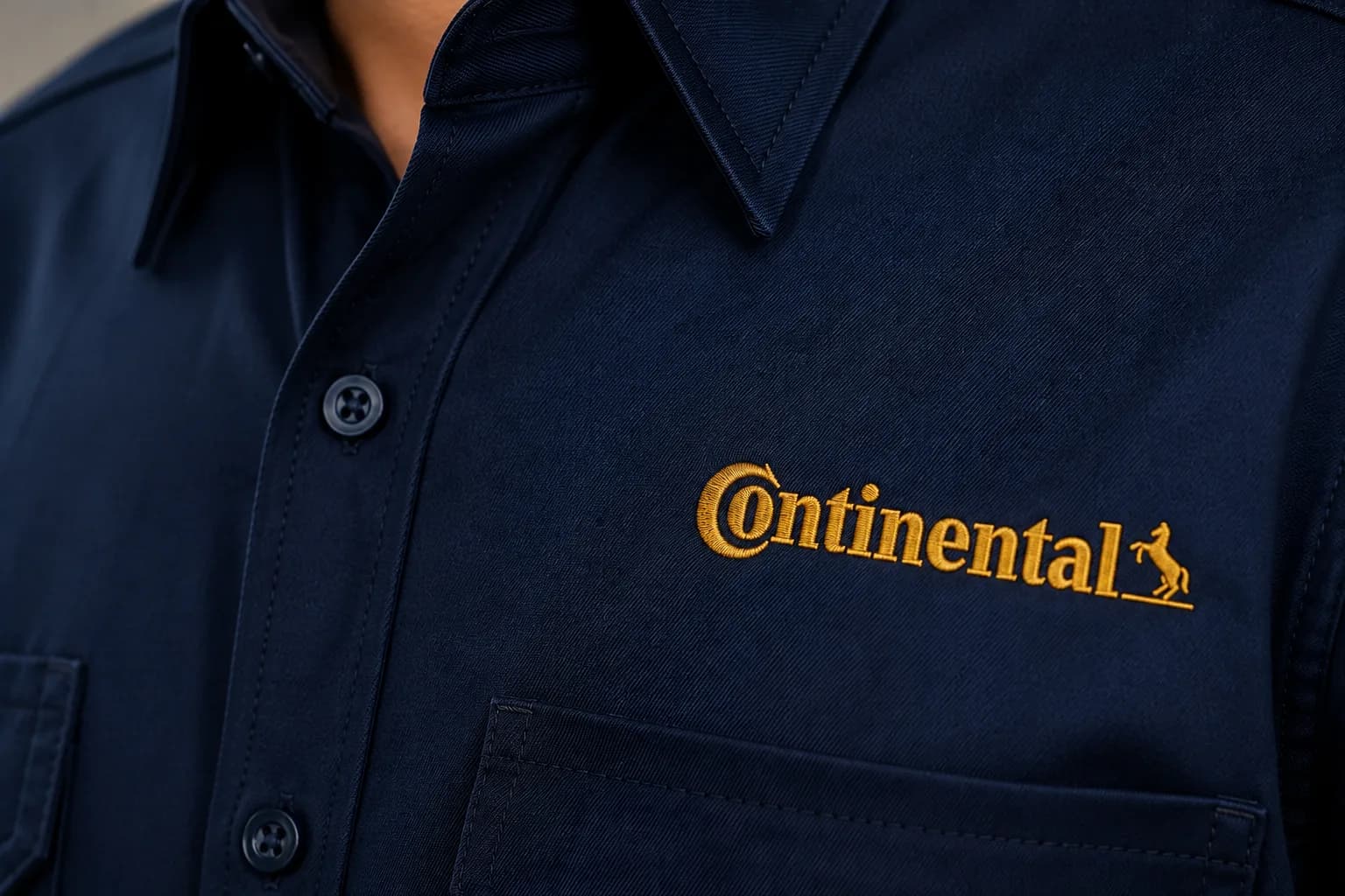 Camisola industrial azul marino con el logo de Continental bordado en hilo dorado, en primer plano mostrando el detalle de la puntada.